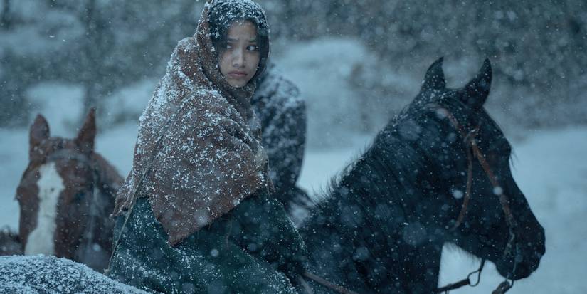 Shawnee Pourier looks behind on horseback in falling snow in American Primeval. 