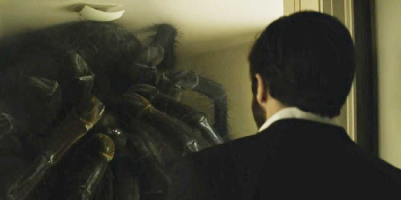 Jake Gyllenhaal with his back to the camera looking at a giant spider in Enemy