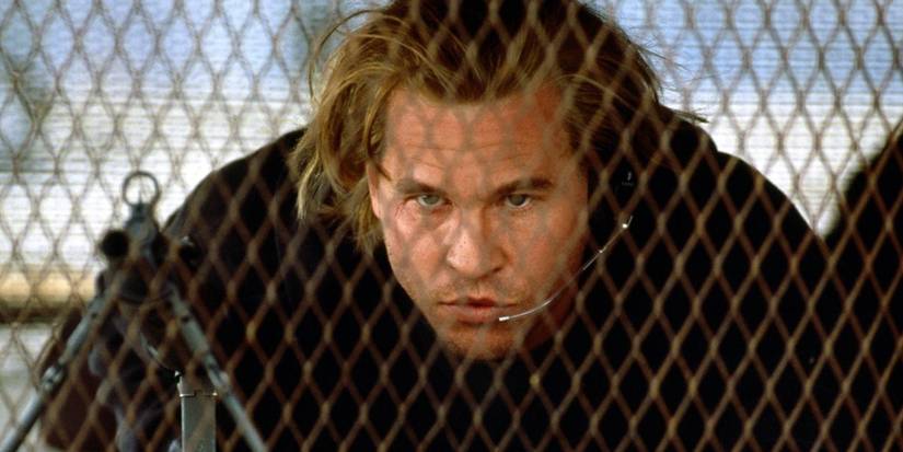 Val Kilmer behind a fence ready to aim a weapon in Heat