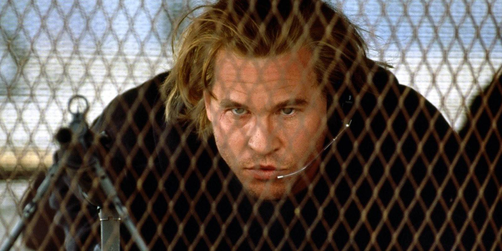 Val Kilmer behind a fence ready to aim a weapon in Heat