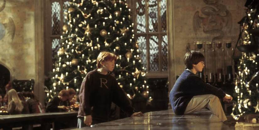 Ron and Harry sit on a table in front of a decorated Christmas tree in 'Harry Potter and the Sorcerer's Stone'