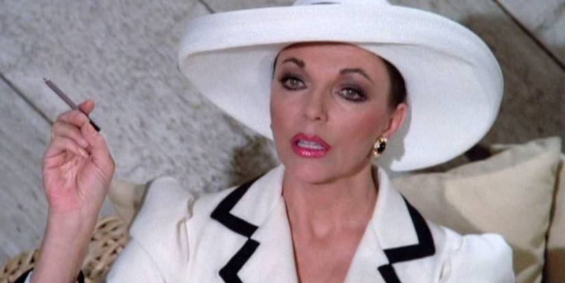 Alexis, wearing a white suit, looks at someone off-screen in Dynasty.