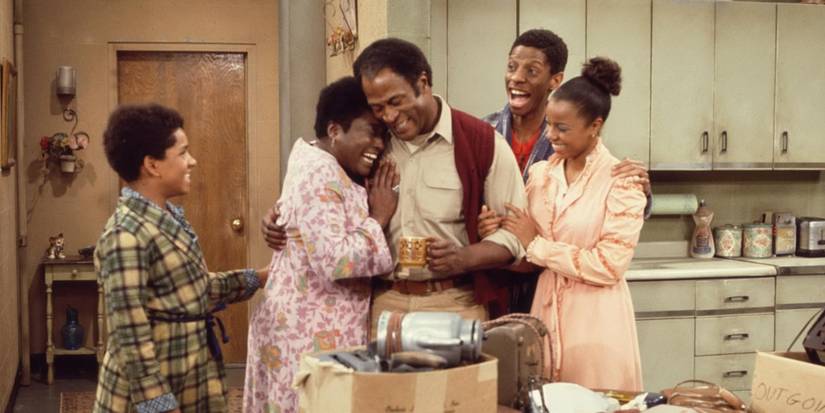 John Amos smiles in the center being embraced by smiling cast members in Good Times.