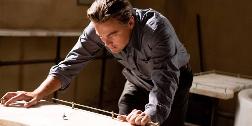 Leonardo DiCaprio dengan penuh perhatian mengamati gasing yang berputar di atas meja di Inception.