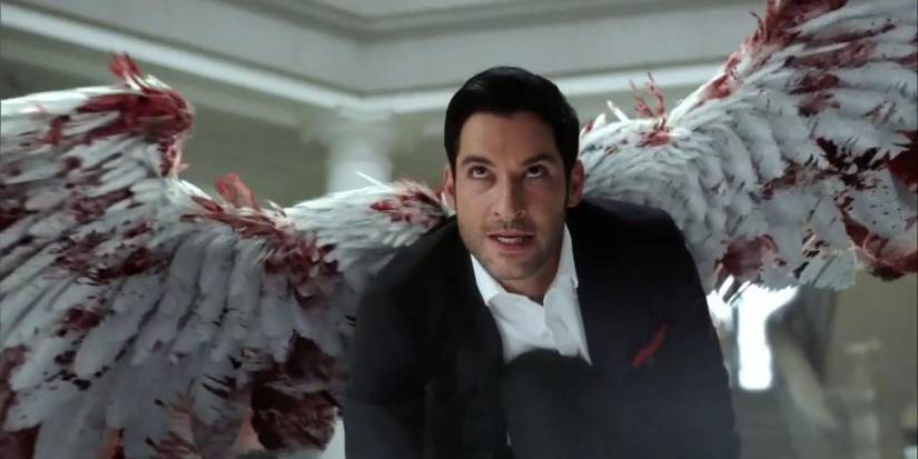 Tom Ellis as Lucifer looking at someone off camera with his angel wings covered in blood in Lucifer