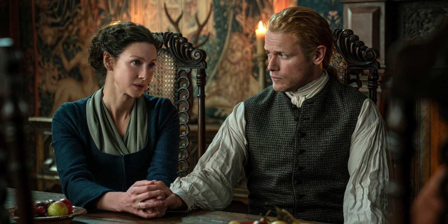 Caitriona Balfe as Claire sitting at a table with Sam Heughan as Jamie in Season 7 Pt 2 of Outlander