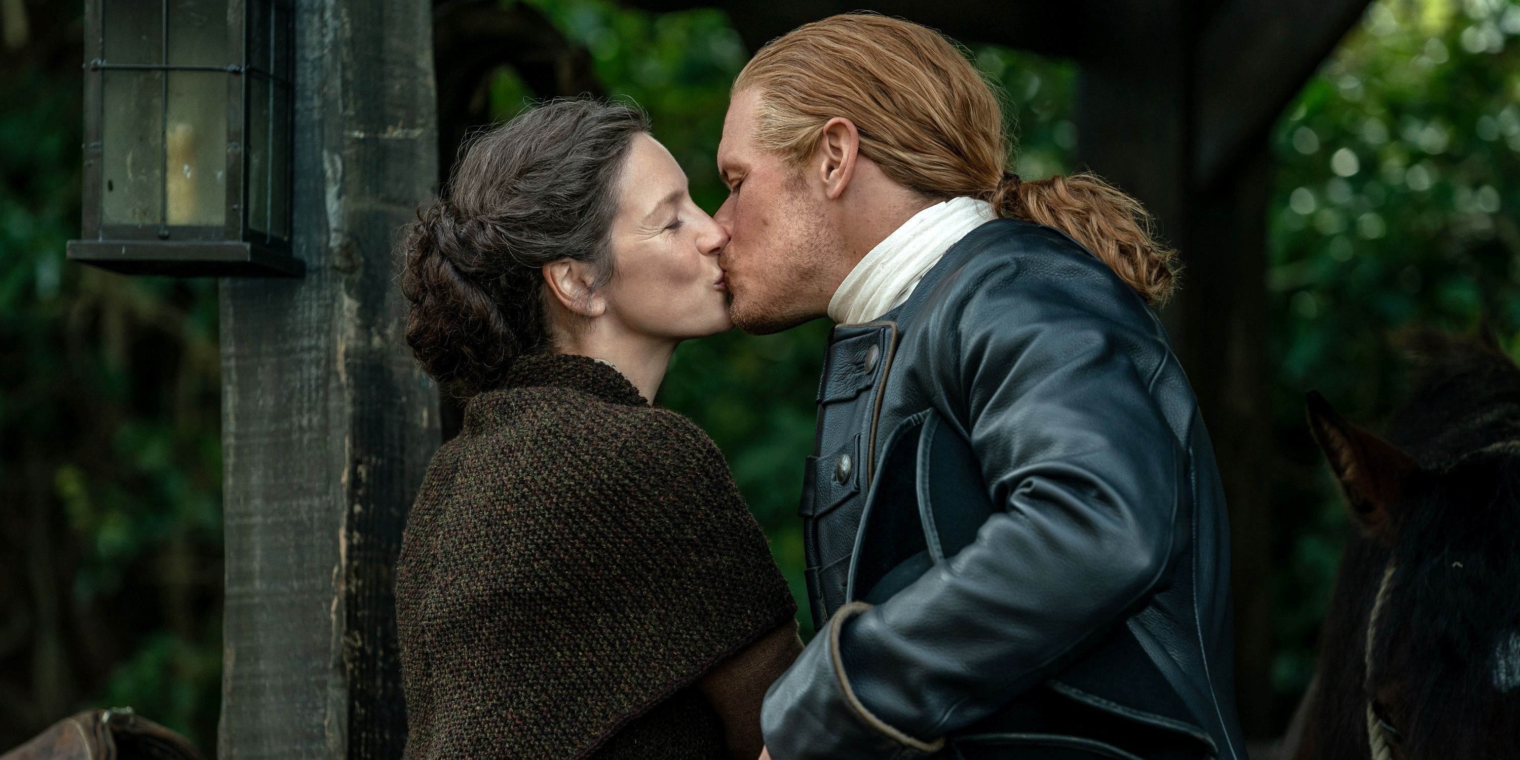 Caitriona Balfe as Claire standing outside and kissing Sam Heughan as Jamie in Season 7 Pt 2 of Outlander