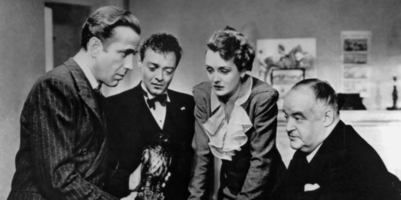 Humphrey Bogart, Peter Lorre, Mary Astor, and Sydney Greenstreet look at a metal bird in The Maltese Falcon