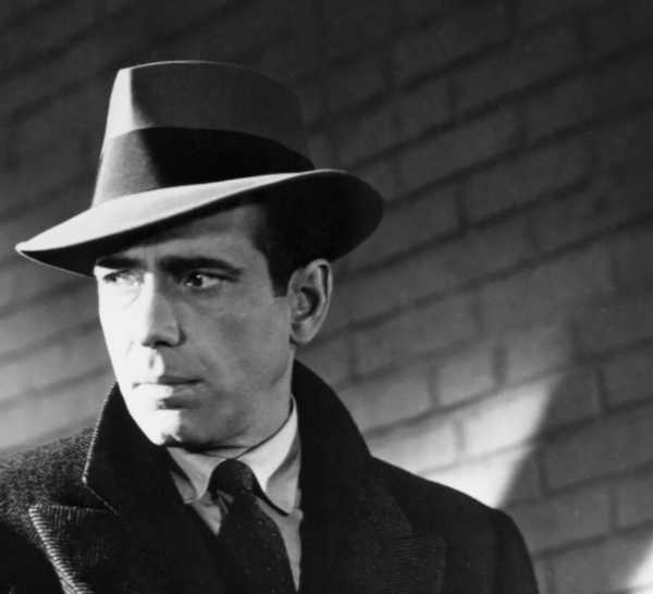 Humphrey Bogart as Sam Spade wearing a hat, trenchcoat, and tie in 'The Maltese Falcon'.