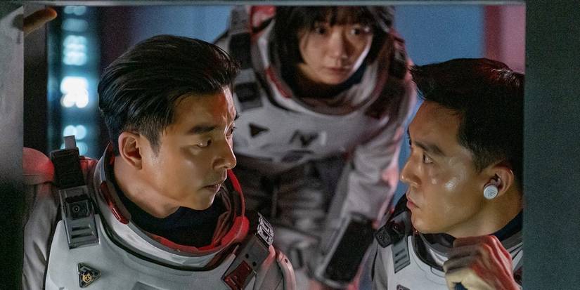 Captain Han (Gong Yoo) on the left staring at Lieutenant Ryu Tae-seok (Lee Joon) on the right with Doctor Song (Bae Doona) standing behind them and watching in The Silent Sea