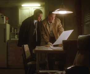 Tony Dinozzo and Timothy Mcgee look at papers on a kitchen table in a dingey apartment in NCIS