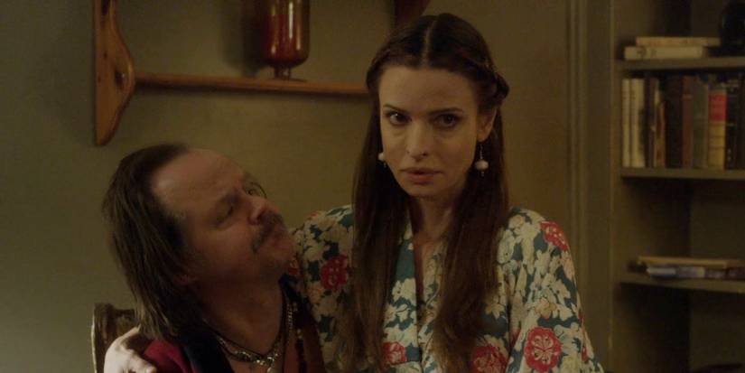 Lisa Marie wearing a long floral 70s dress while sitting on Larry Fessenden's lap in "We Are Still Here"