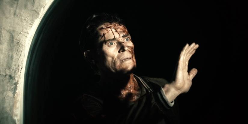 Willem Dafoe standing in a large waterpipe with blood on his face, holding his hand up against the sun in 'Daybreakers'