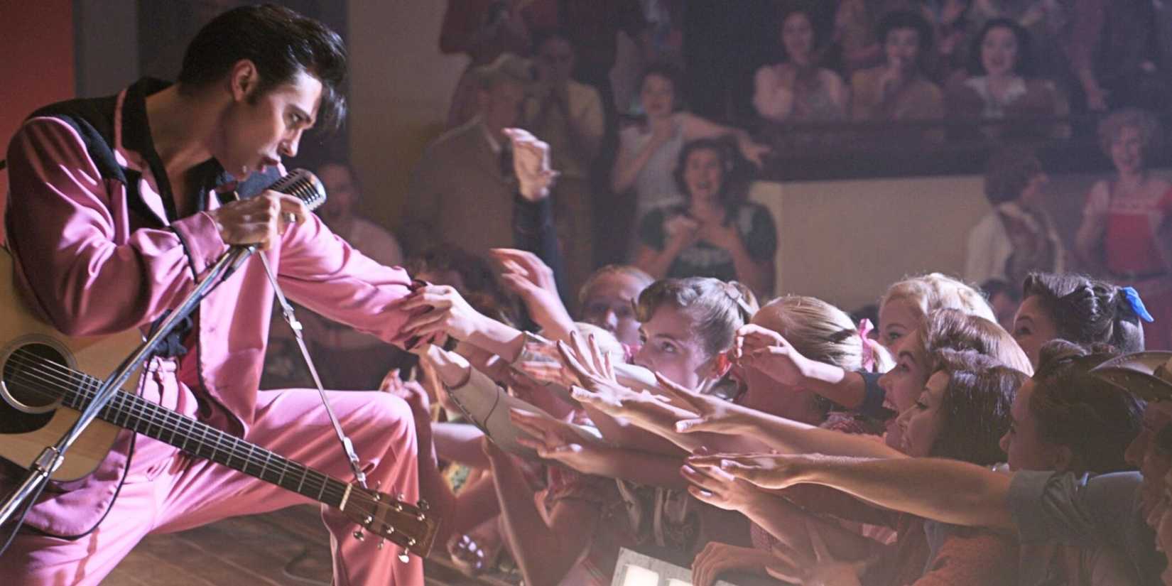 Austin Butler as Elvis Presley kneeling on stage and reaching out to fans in Elvis (2022).