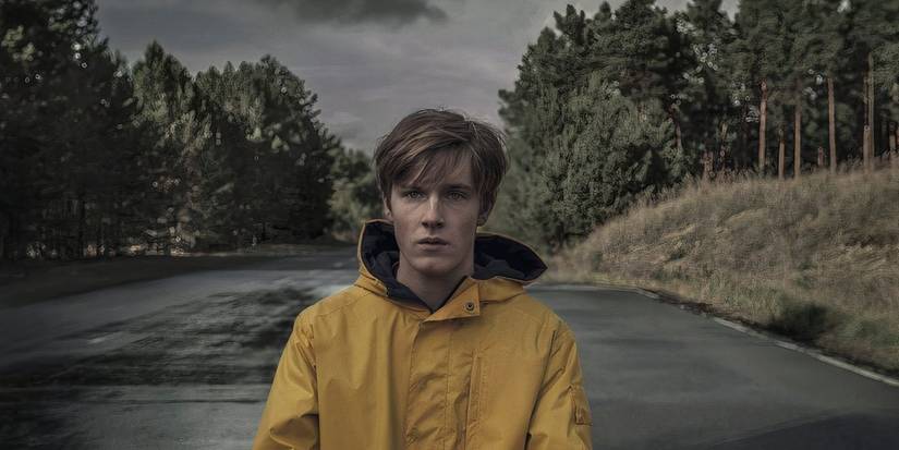 Louis Hofmann standing on a paved road in the woods in Dark.