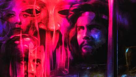 King Arthur, played by actor Nigel Terry, stands with a sword in his hand, looking towards ghoulish faces cast in a pink light.