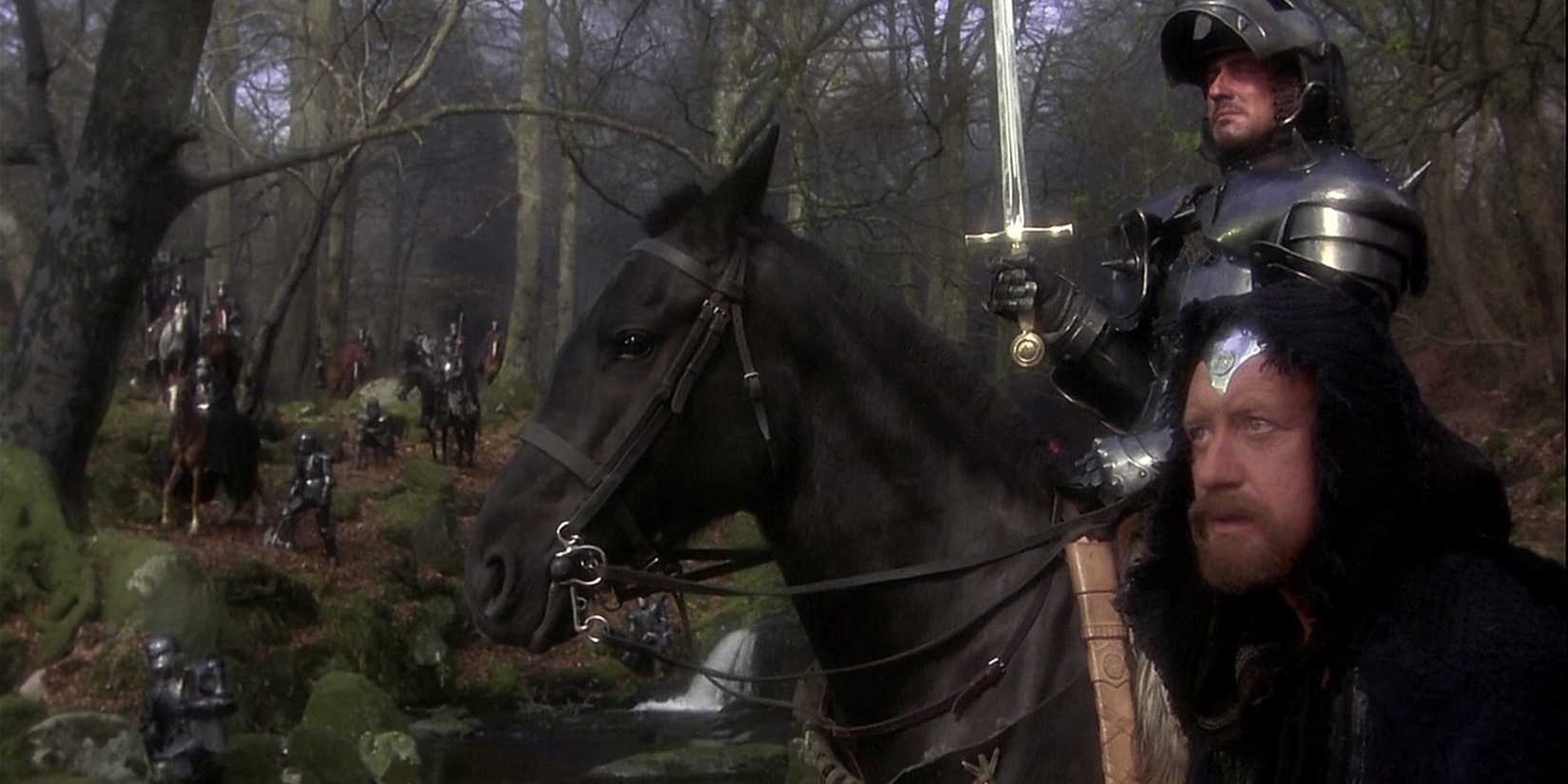 Nicol Williamson as Merlin stands next to a knight on horseback in the forest in 'Excalibur' *(1981)