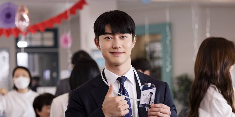 A man in a work suit holds his work badge and a thumb up at an office party in Gaus Electronics.