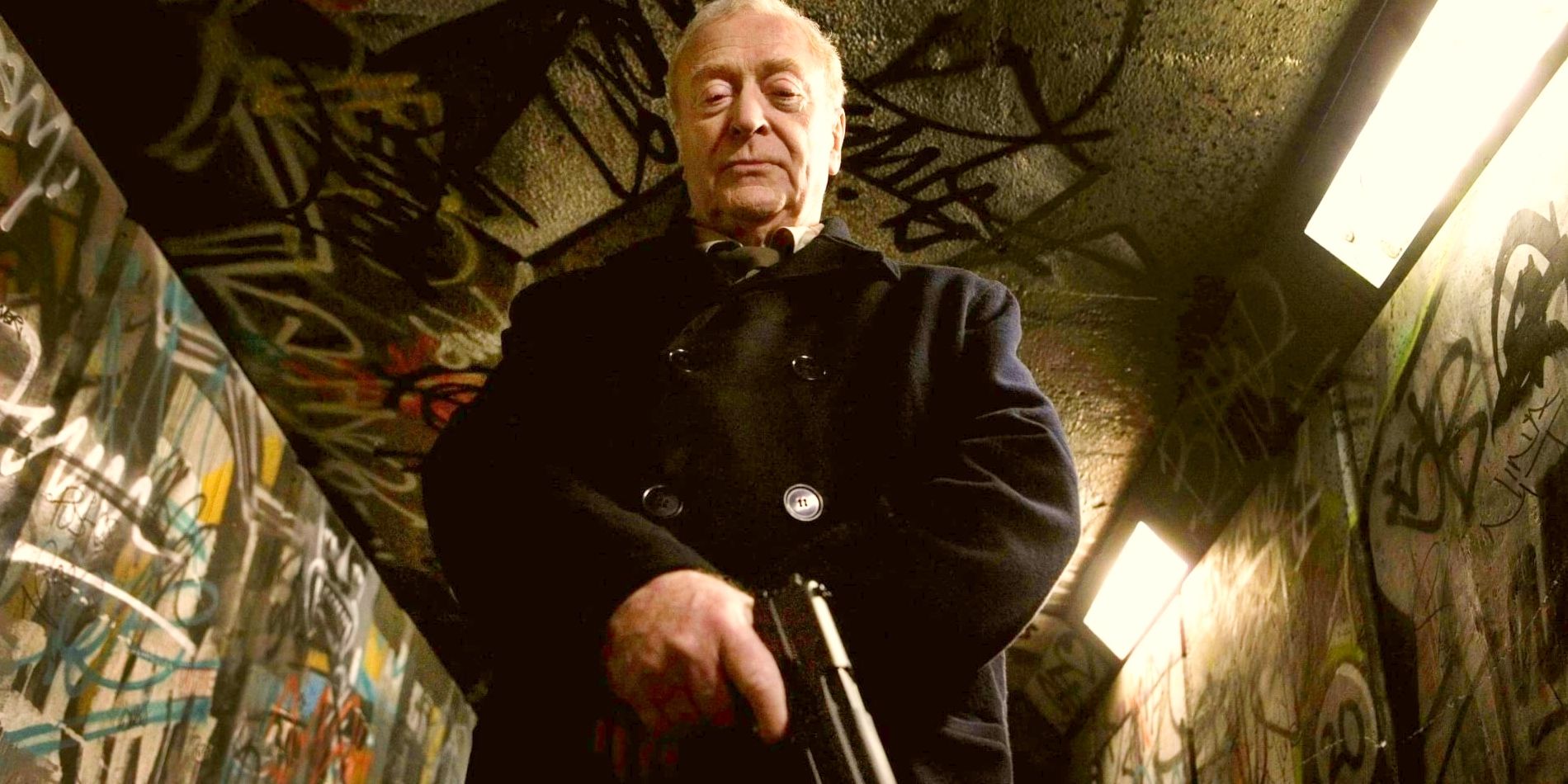 Michael Caine as Harry Brown, standing in a graffitied underpass holding a gun.