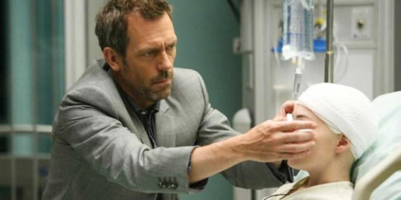 Hugh Laurie tending to a patient's eye who is sitting up in a hospital bed in House episode Birthmarks
