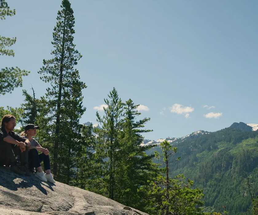 Jack and Mel sitting on a rock surrounded by stunning nature in 'Virgin River'