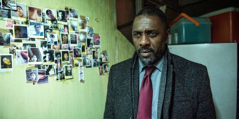 Idris Elba as Luther standing next to a wall of pictures while looking worried in Luther. 
