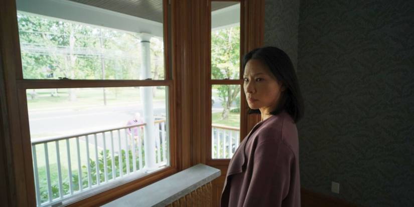 Rebekah stands somewhat disheveled at a large window in Presence