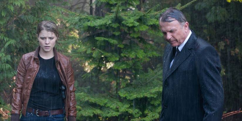 Rebecca Madsen (Sarah Jones) and Emerson Hauser (Sam Neill) are drenched and looking down at something in the forest in Alcatraz.