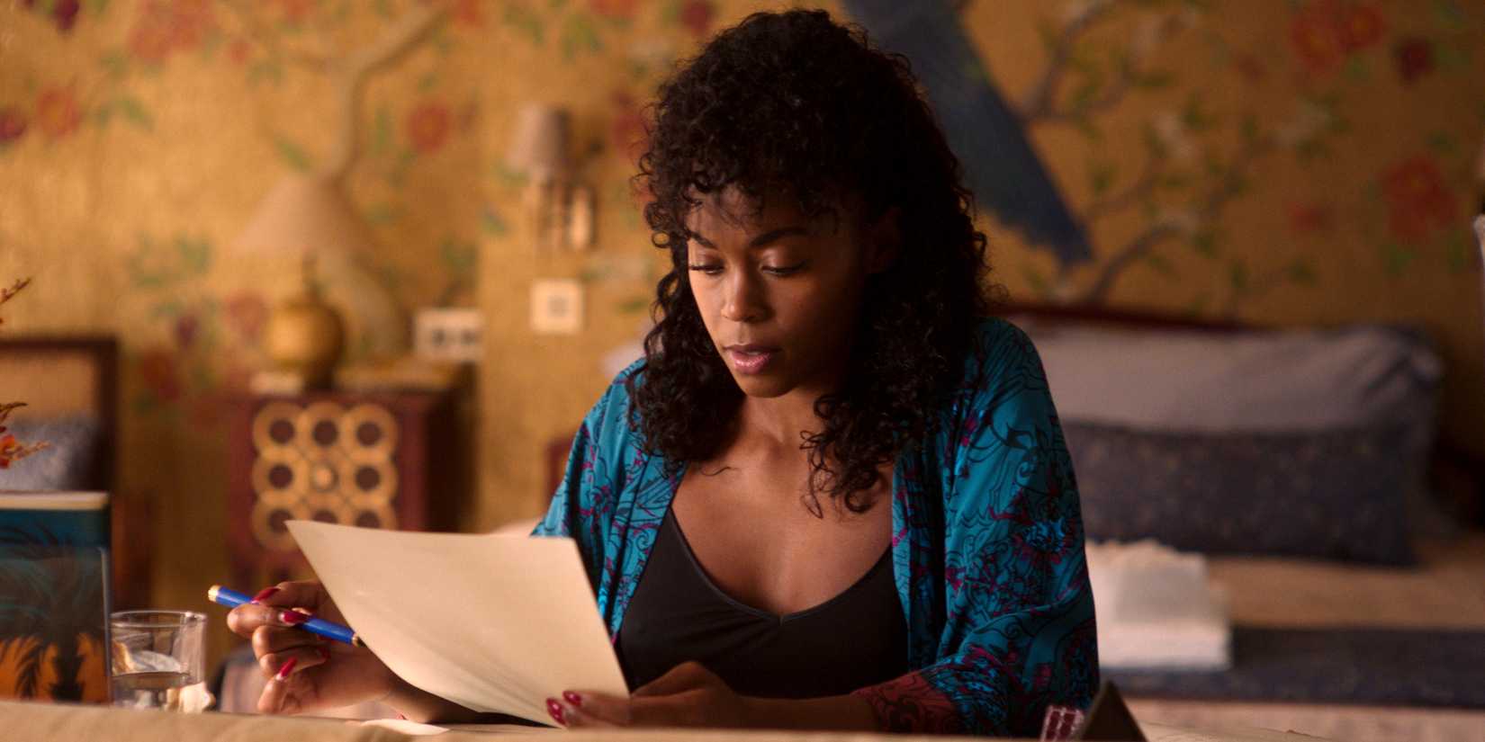 Nafessa Williams as Cameron Cook sitting and looking down at a piece of paper in Rivals