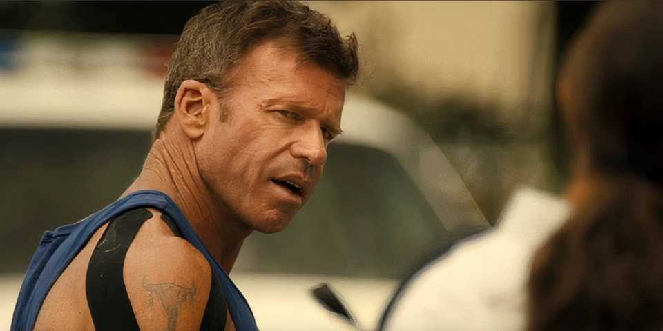 Taylor Sheridan as Cody Spears in a tanktop looking at someone to his right and talking to them in Lioness.