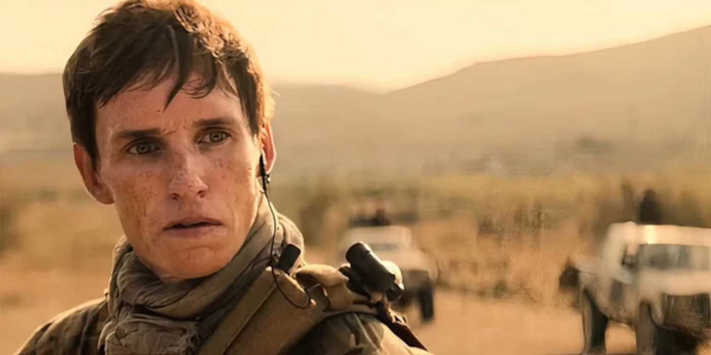 Çakal olarak Eddie Redmayne, çöl gününde askeri üniformalı giyinmiş çölde duruyor.