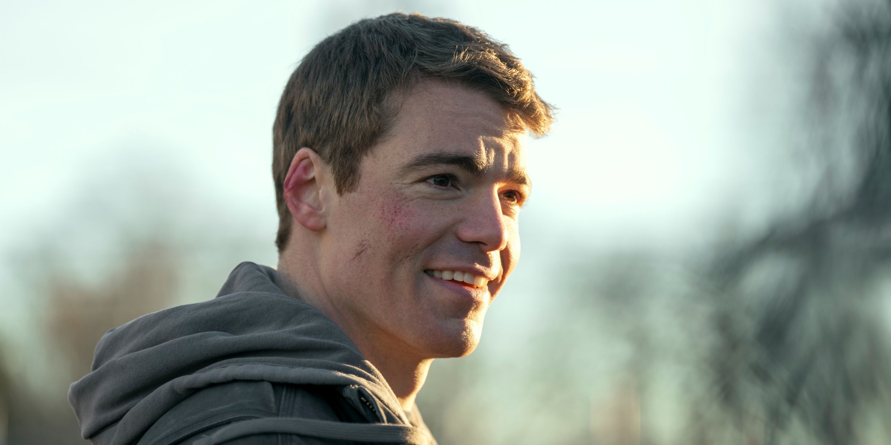 Gabriel Basso sebagai Peter tersenyum sambil melihat dari balik bahu kanannya di Musim 2 The Night Agent