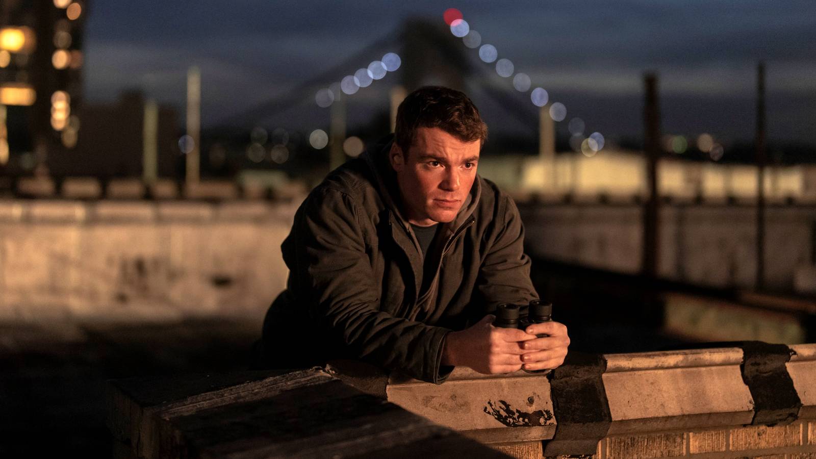 Gabriel Basso as Peter Sutherland leaning on a wall outside in Season 2 of The Night Agent