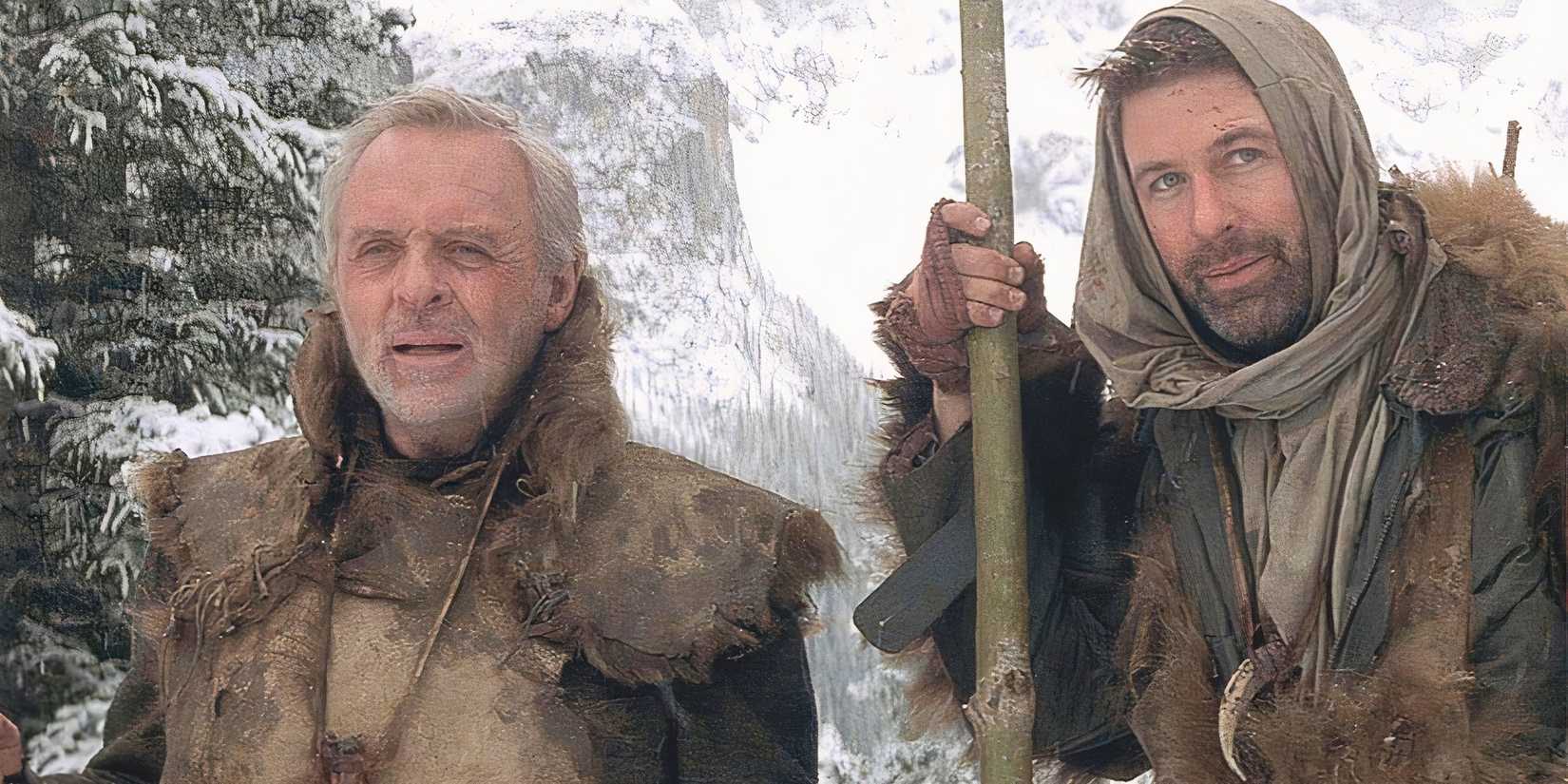 Anthony Hopkins and Alec Baldwin standing next to each other in a snow covered forest in The Edge (1997).