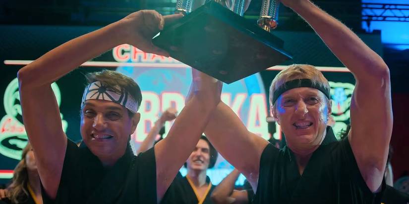 Daniel LaRusso (Ralph Macchio) and Johnny Lawrence (William Zabka) holding up the Sekai Taikai trophy in Cobra Kai