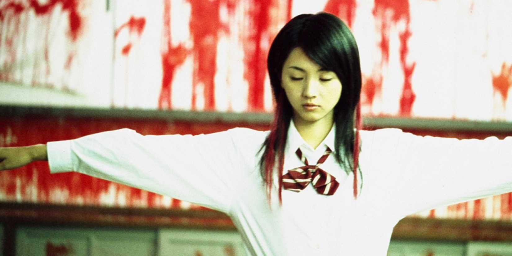 A young woman stands in a bloody room with her arms outstretched in Love Exposure.