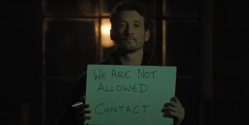 Miles Teller, holding up a sign that says "We Are Not Allowed Contact", as Levi in 'The Gorge'