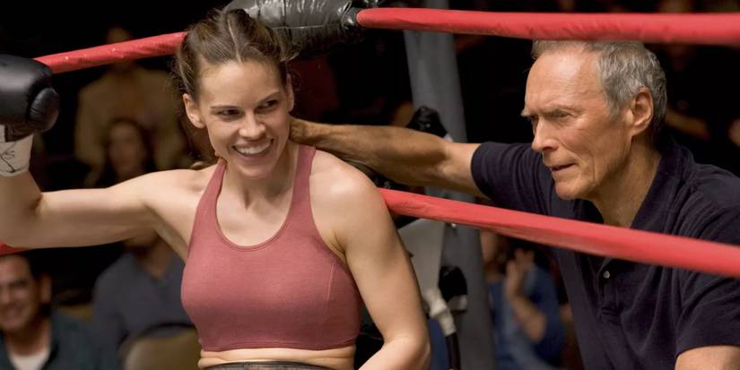 Hilary Swank smiling, sitting in a boxing ring as Clint Eastwood stands nearby in Million Dollar Baby.
