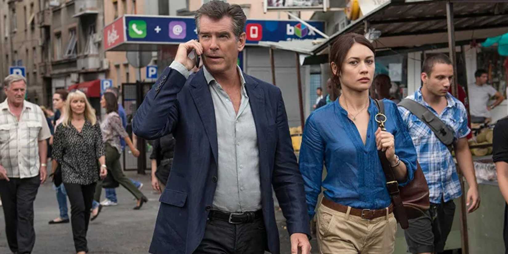 Pierce Brosnan on the phone while walking with Olga Kurylenko in a crowd of people in The November Man (2014)