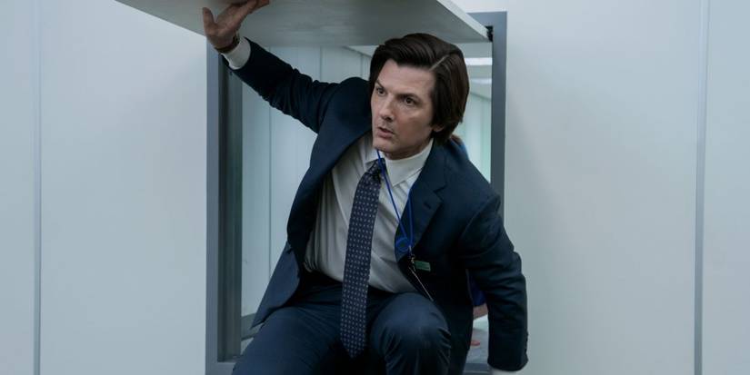 Adam Scott in a business suit climbs through a small hatch door in Severance Season 2 Episode 3.
