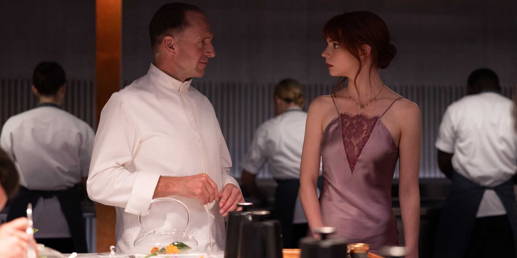 Ralph Fiennes as Chef Julian Slowik and Anya Taylor-Joy as Margot stare at each other in The Menu.