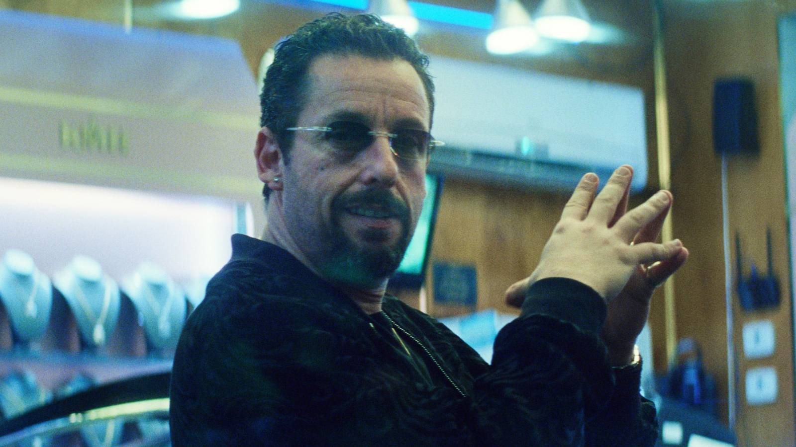 Adam Sandler with sunglasses on looks amused in Uncut Gems.