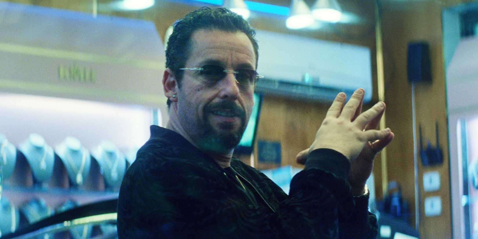 Adam Sandler with sunglasses on looks amused in Uncut Gems.