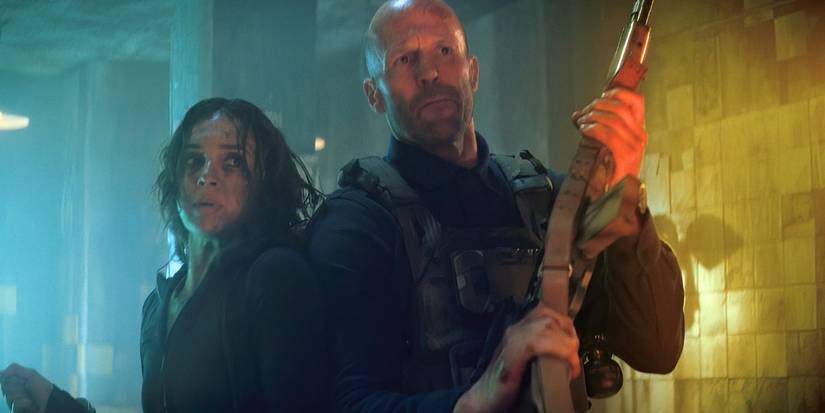Jason Statham'ın Levon Cade, Arianna Rivas Jenny Garcia'nın çalışan bir adamda yanında dururken bir tüfek tuttu.