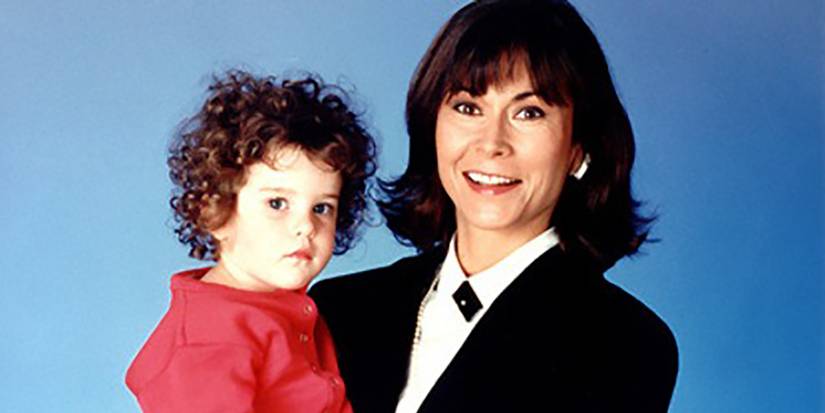 A woman in a suit smiling and holding a toddler on a blue background from Baby Boom.