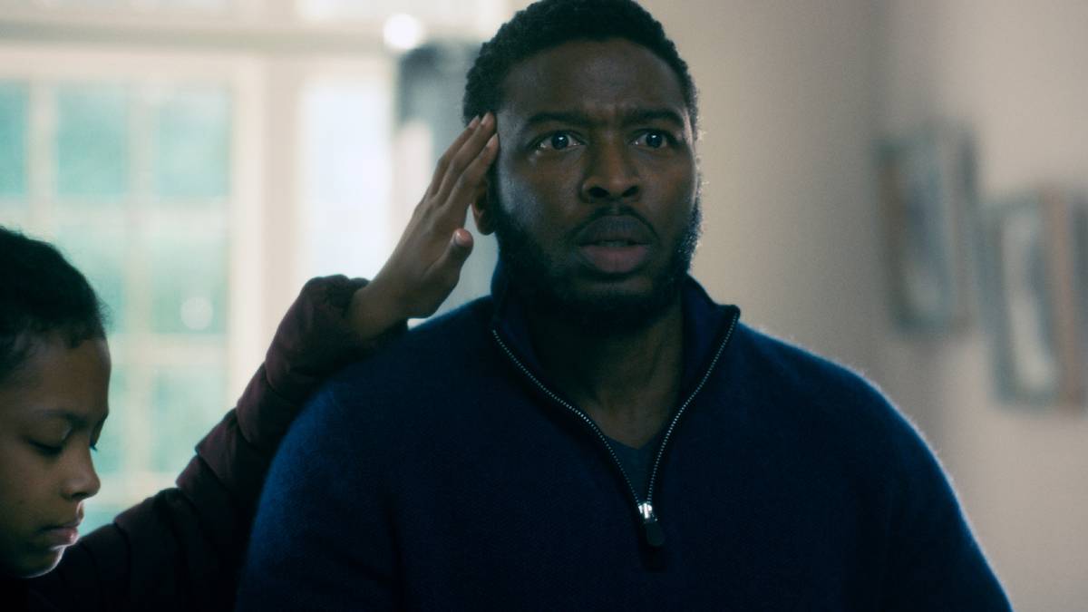 Zackary Momoh looking on in shock while his head is touched by a child in Doctor Sleep