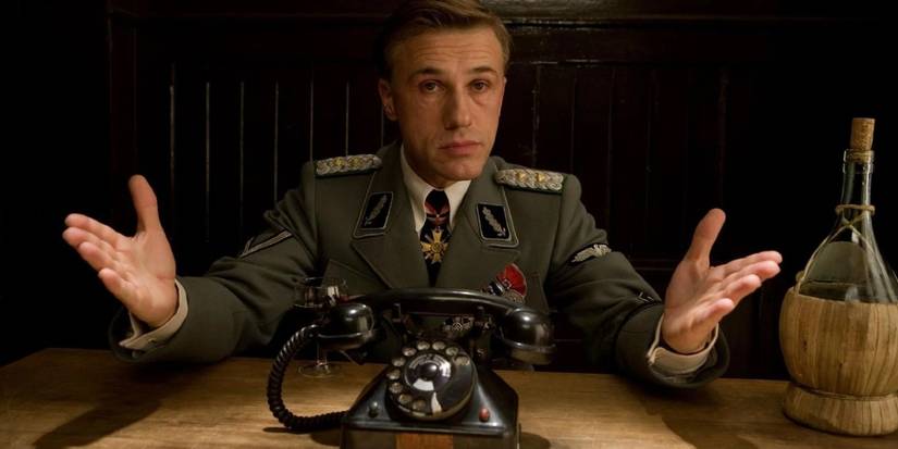 Hans Landa (Christoph Waltz) sitting behind a table and spreading his arms in Inglourious Basterds.