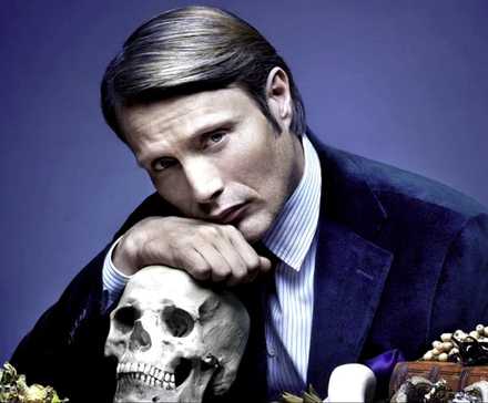 Mads Mikkelsen as Hannibal Lecter resting his chin on a human skull and looking at the camera in Hannibal.