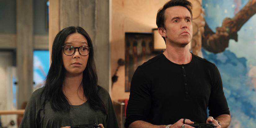 Charlotte Nicdao as Poppy standing next to Rob McElhenney as Ian playing video games in Mythic Quest.