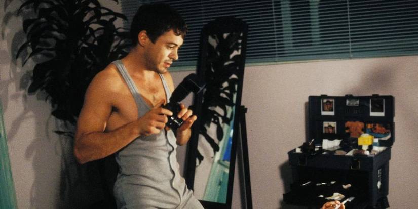 Robert Downey Jr. on a bed in a onesie holding a camera in Short Cuts